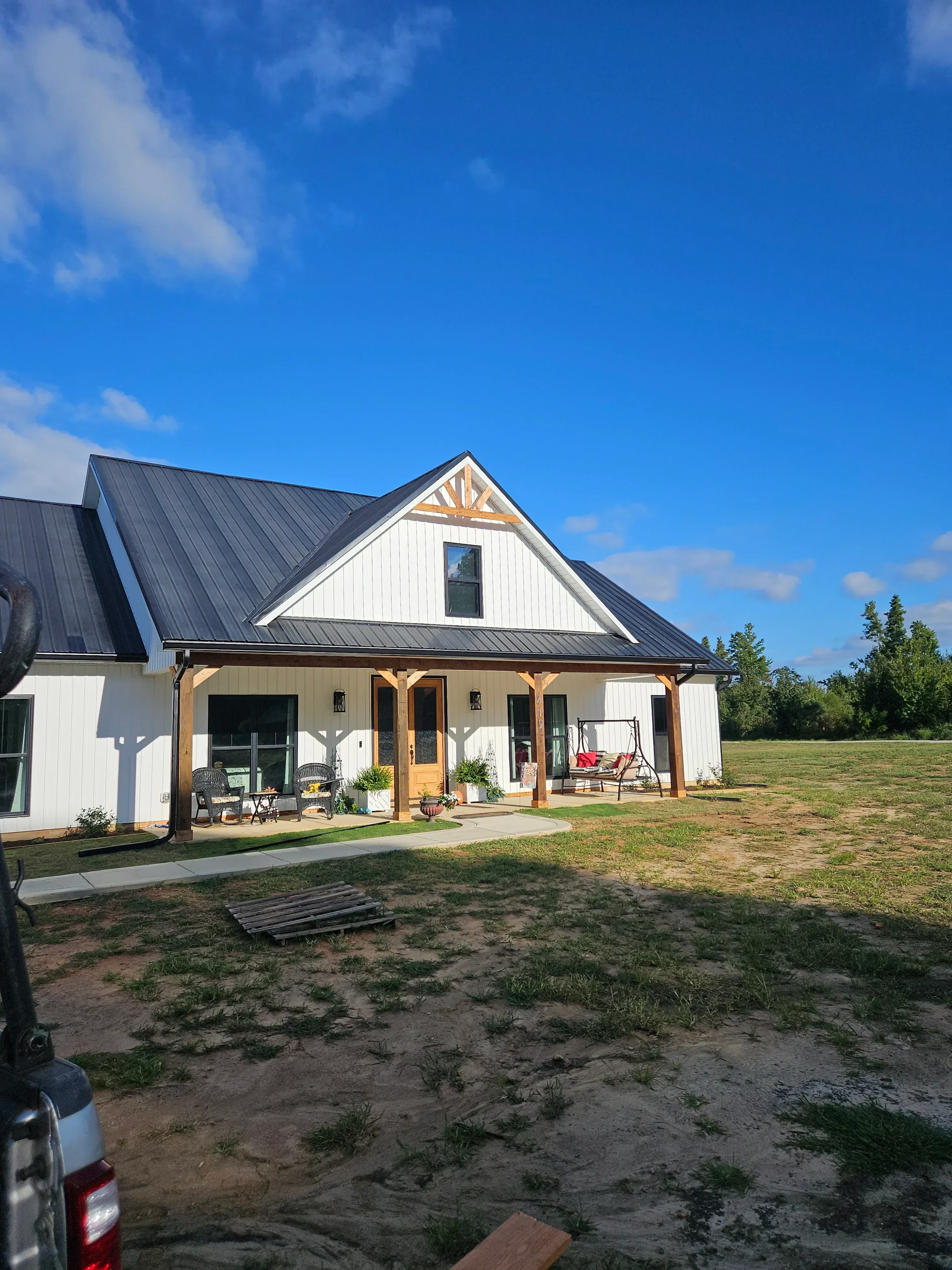 Dark metal standing-seam roof with white siding, wood deck framing, and new window installations on modern home
